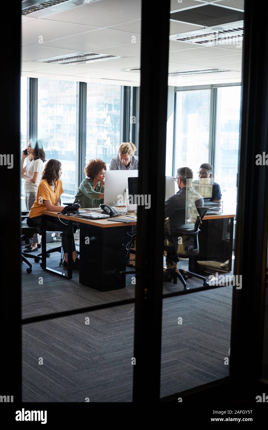 L'équipe d'affaires créatifs travaillant dans un bureau temporaire, vu à partir de la porte à travers la paroi de verre, vertical Banque D'Images