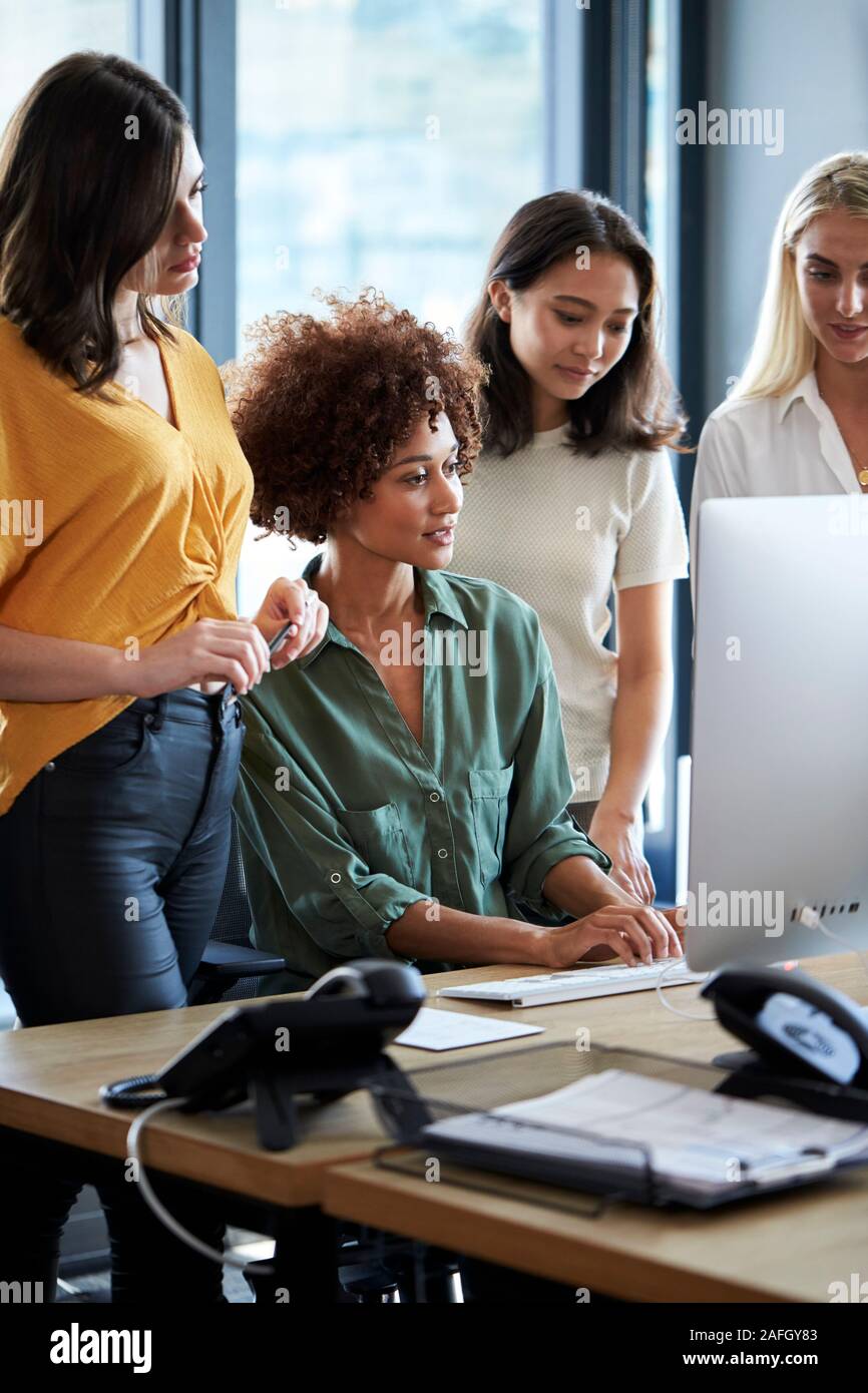 Quatre femmes créatifs travaillant autour de l'écran d'un ordinateur dans un bureau, vue latérale, verticale, Close up Banque D'Images