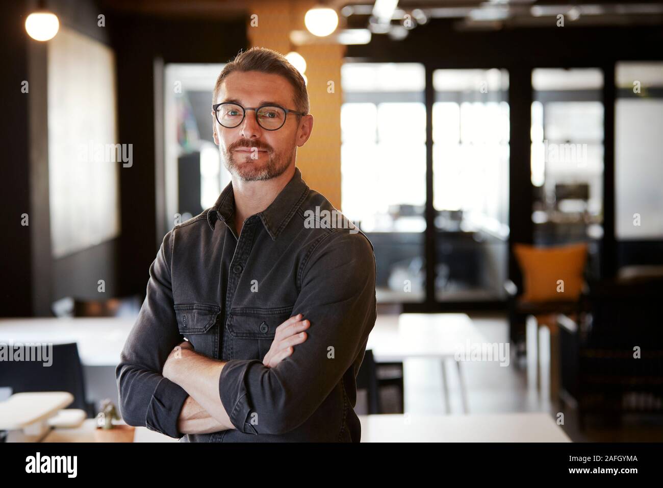 Homme de race blanche d'âge moyen portant des lunettes créative dans un bureau permanent à la recherche d'appareil photo, jusqu'à la taille Banque D'Images