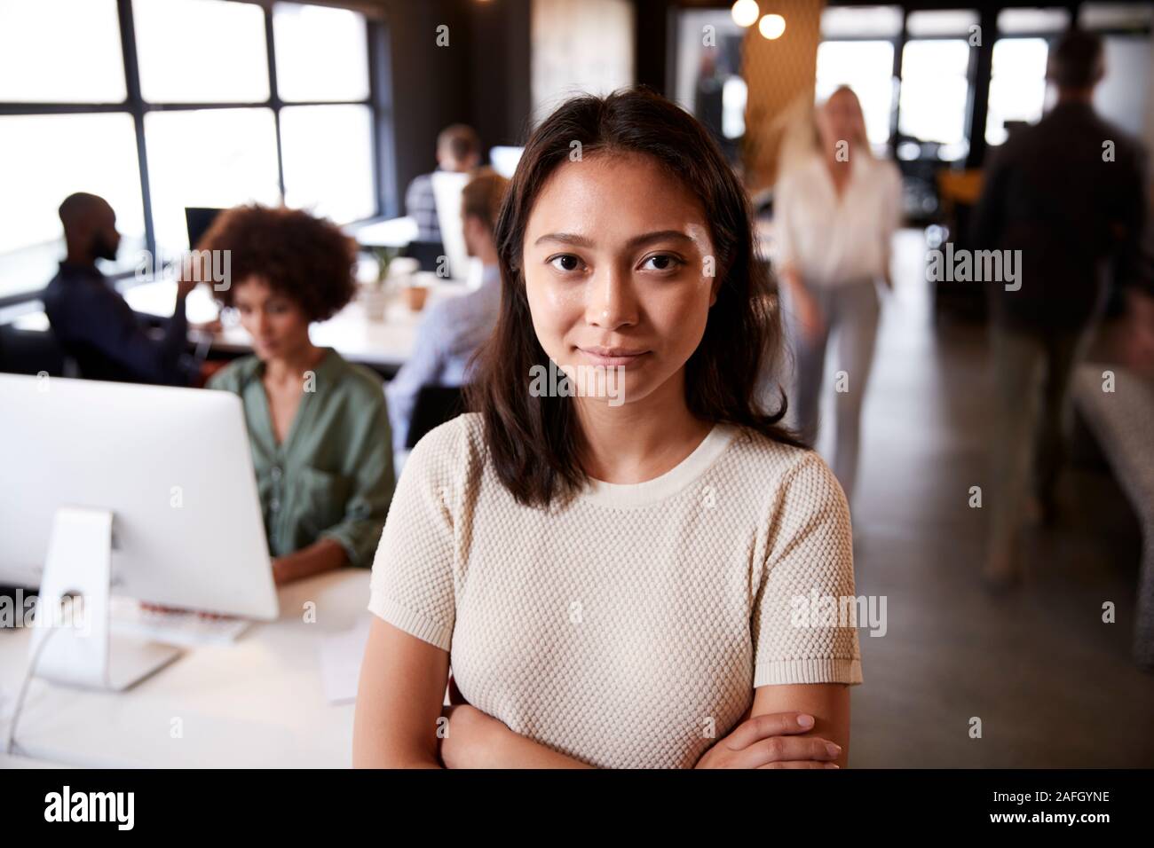 Femme Asiatique millénaire creative debout dans un bureau temporaire occupé, souriant à l'appareil photo Banque D'Images