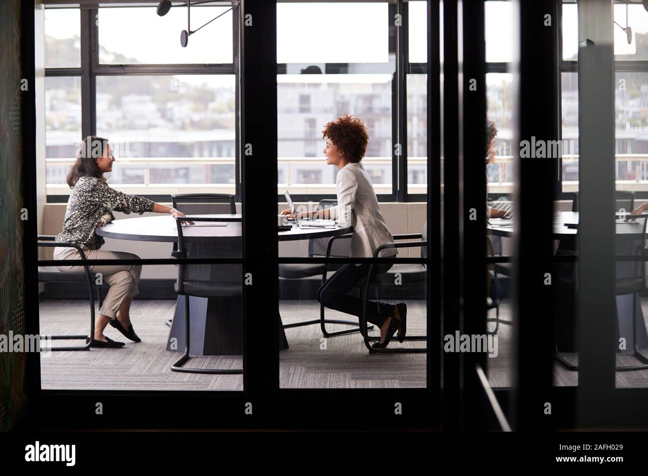 Deux femmes d'millénaire réunion pour une entrevue d'emploi, pleine longueur, vu à travers la paroi de verre Banque D'Images