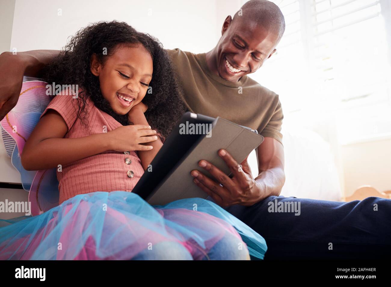 Le père et sa fille assis sur le lit dans une chambre d'enfant Using Digital Tablet Together Banque D'Images