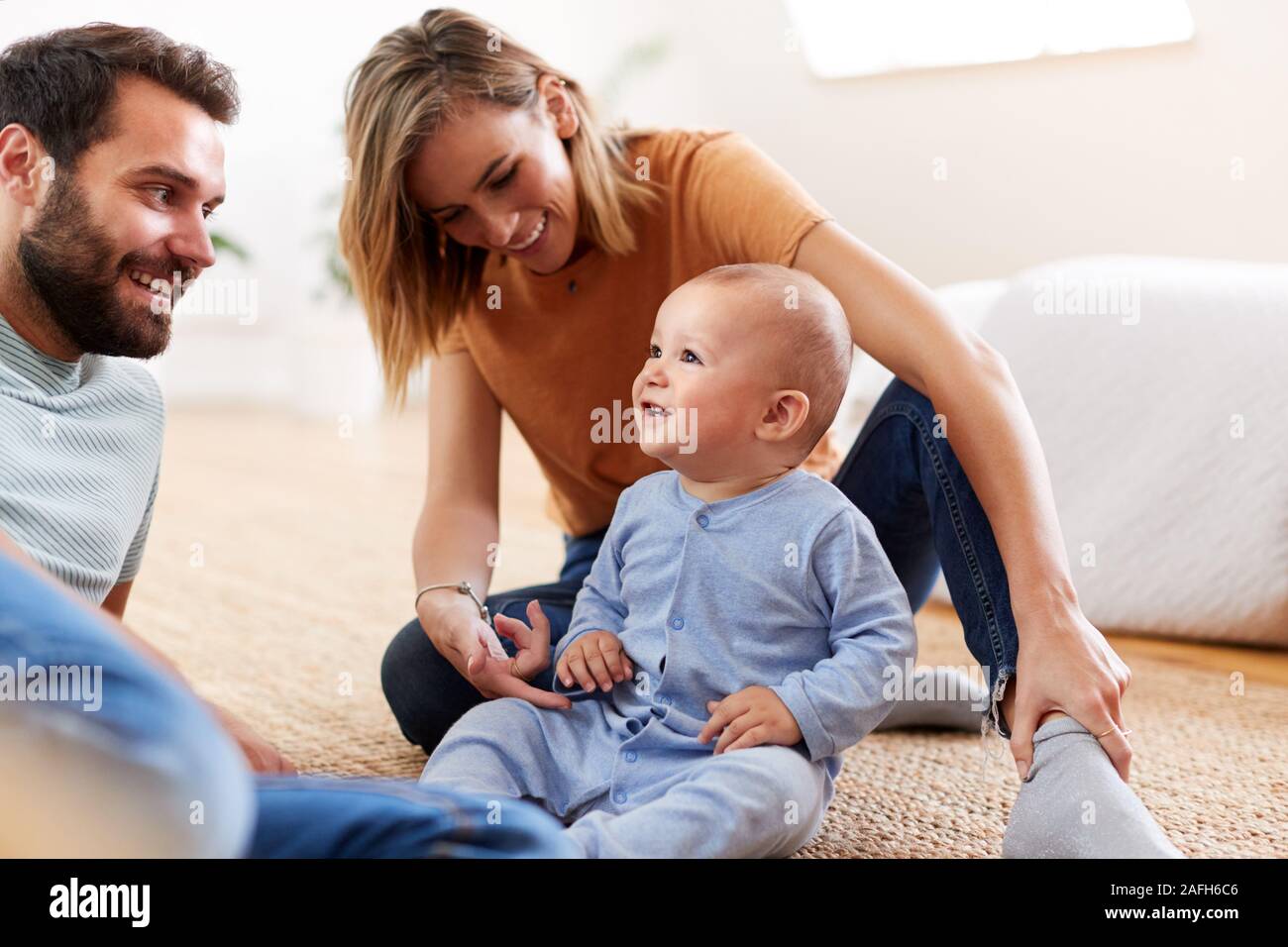 Les parents assis sur le plancher à la maison à jouer avec son bébé Banque D'Images