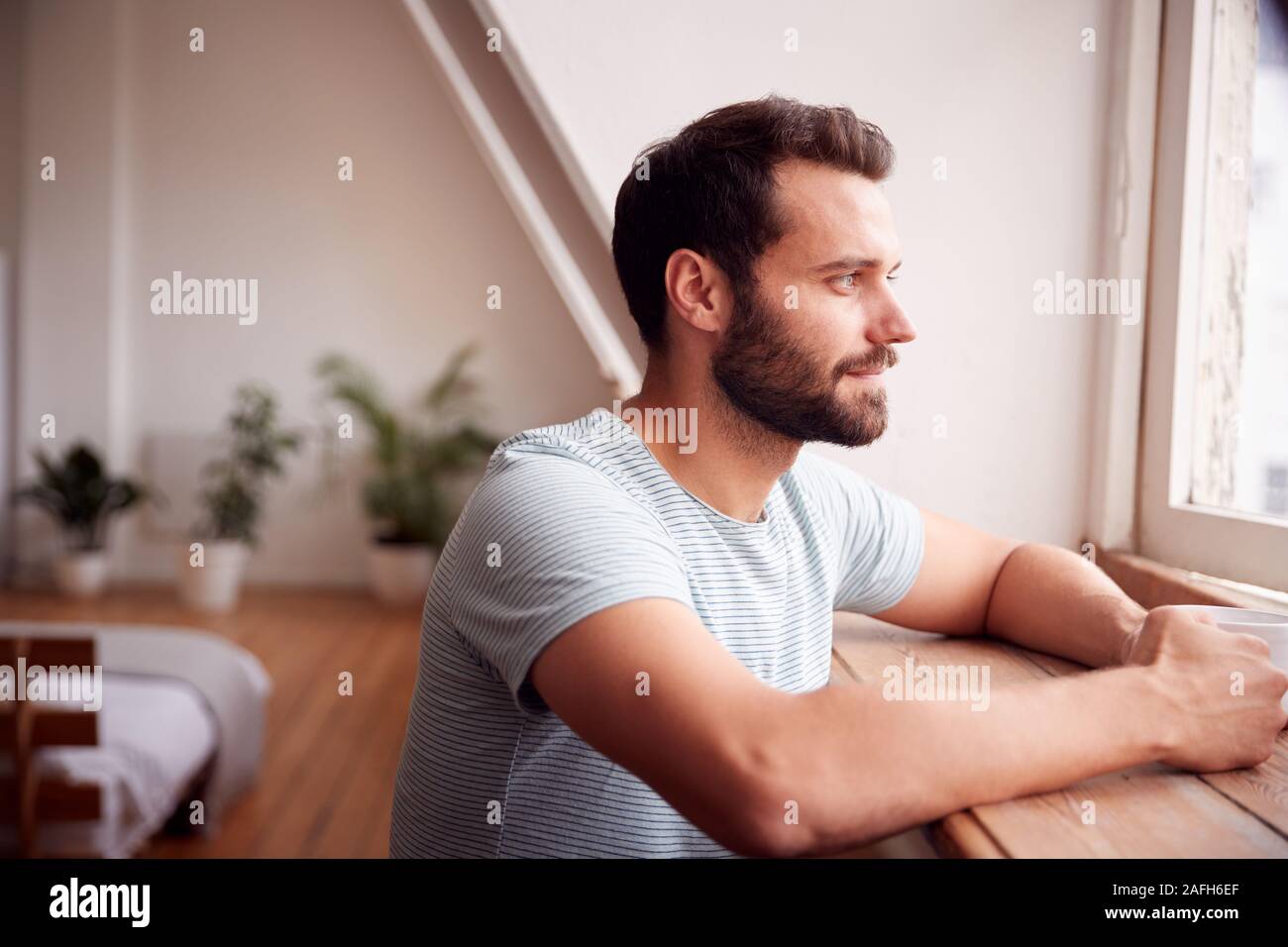 Young Man Relaxing In Loft appartement à hors de fenêtre avec boisson chaude Banque D'Images