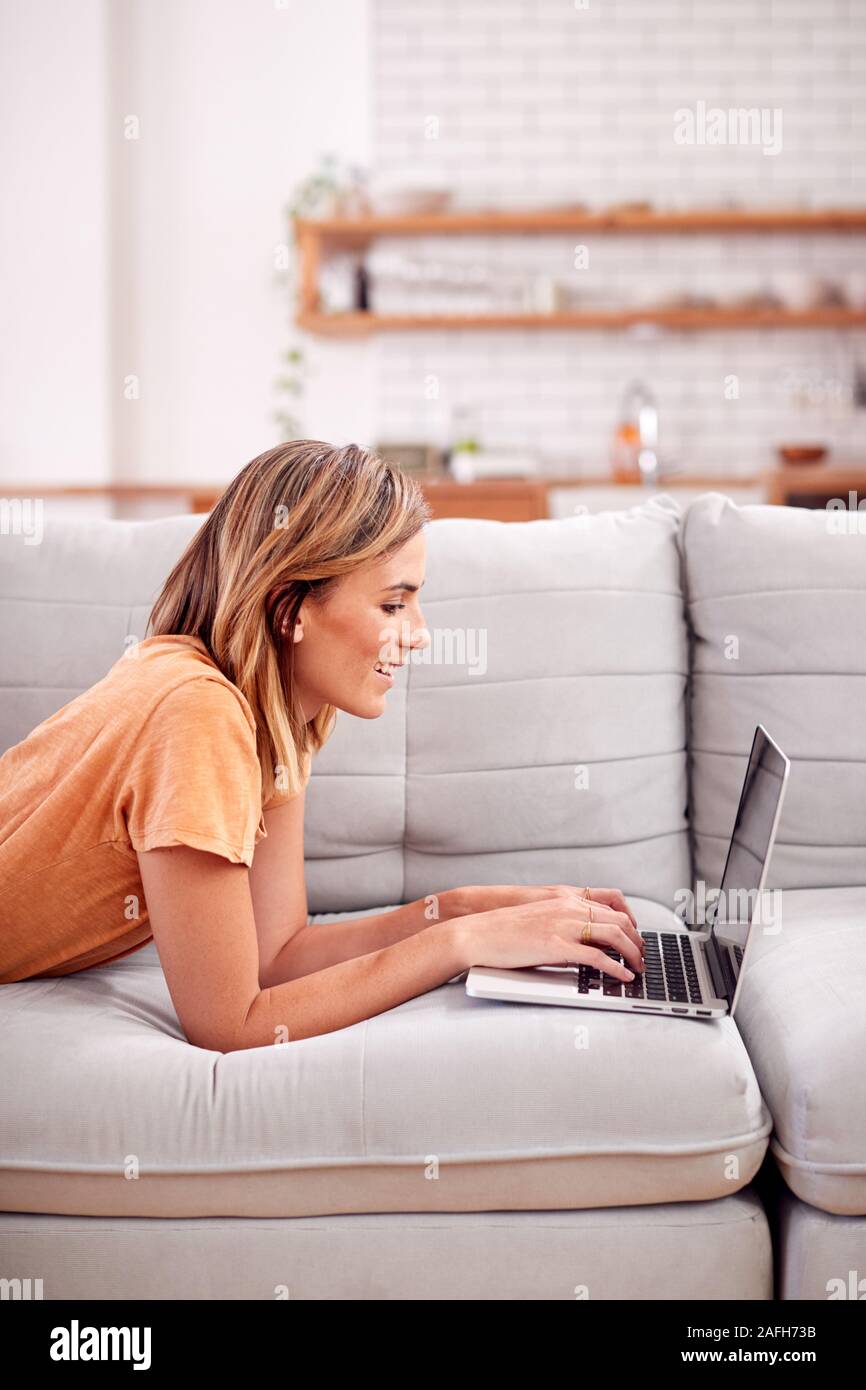 Woman Lying On Sofa At Home Using laptop computer Banque D'Images