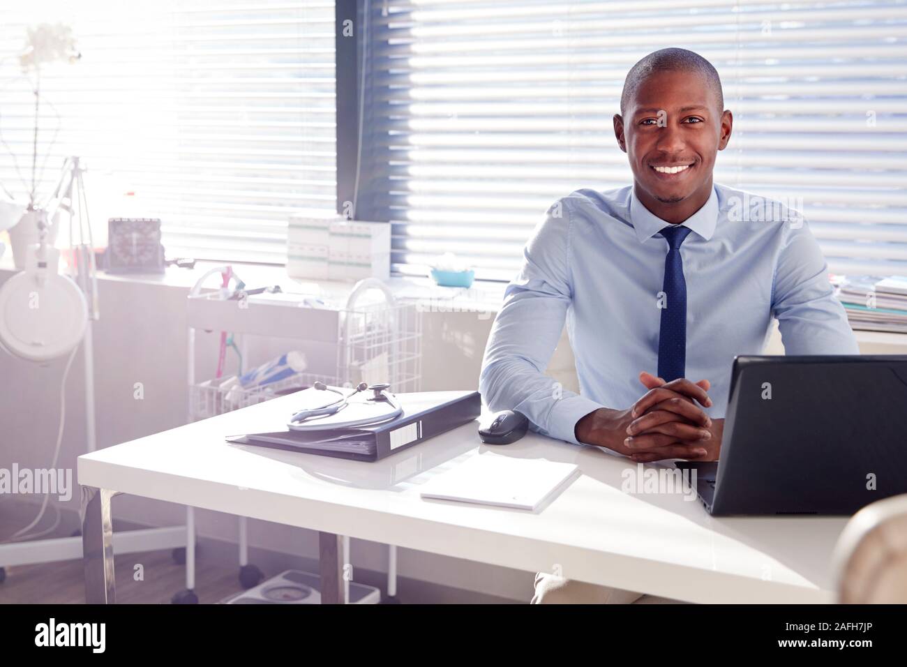 Portrait Of Smiling Male Doctor Sitting Behind Desk In Office Banque D'Images