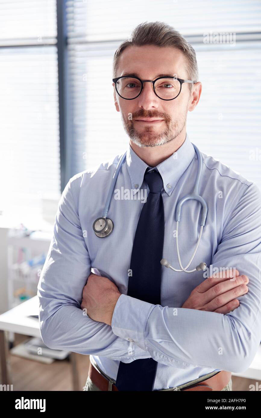 Portrait Of Smiling Mature Male Doctor with Stethoscope Standing By Desk In Office Banque D'Images