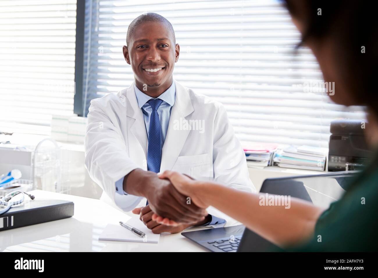 Female Patient Shaking Hands With Doctor Sitting At Desk In Office Banque D'Images