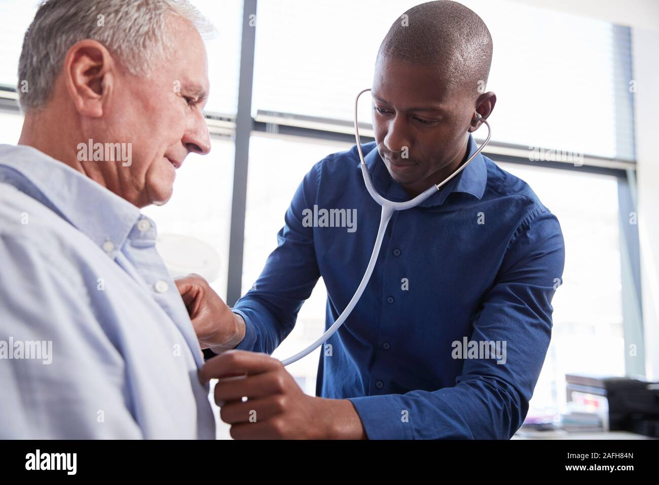 Médecin à l'écoute de la poitrine d'Senior Male Patient pendant l'examen médical in Office Banque D'Images