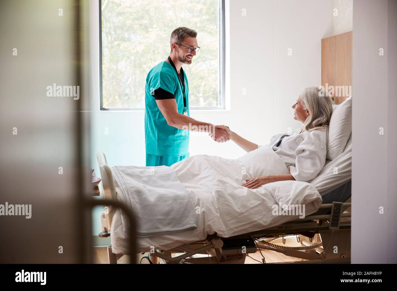 Visiter chirurgien et serrer la main de femme mature Patient In Hospital Bed Banque D'Images