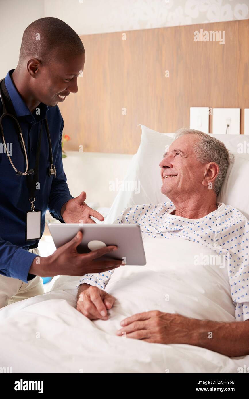 Médecin avec tablette numérique visiter et parler avec Senior Male Patient In Hospital Bed Banque D'Images
