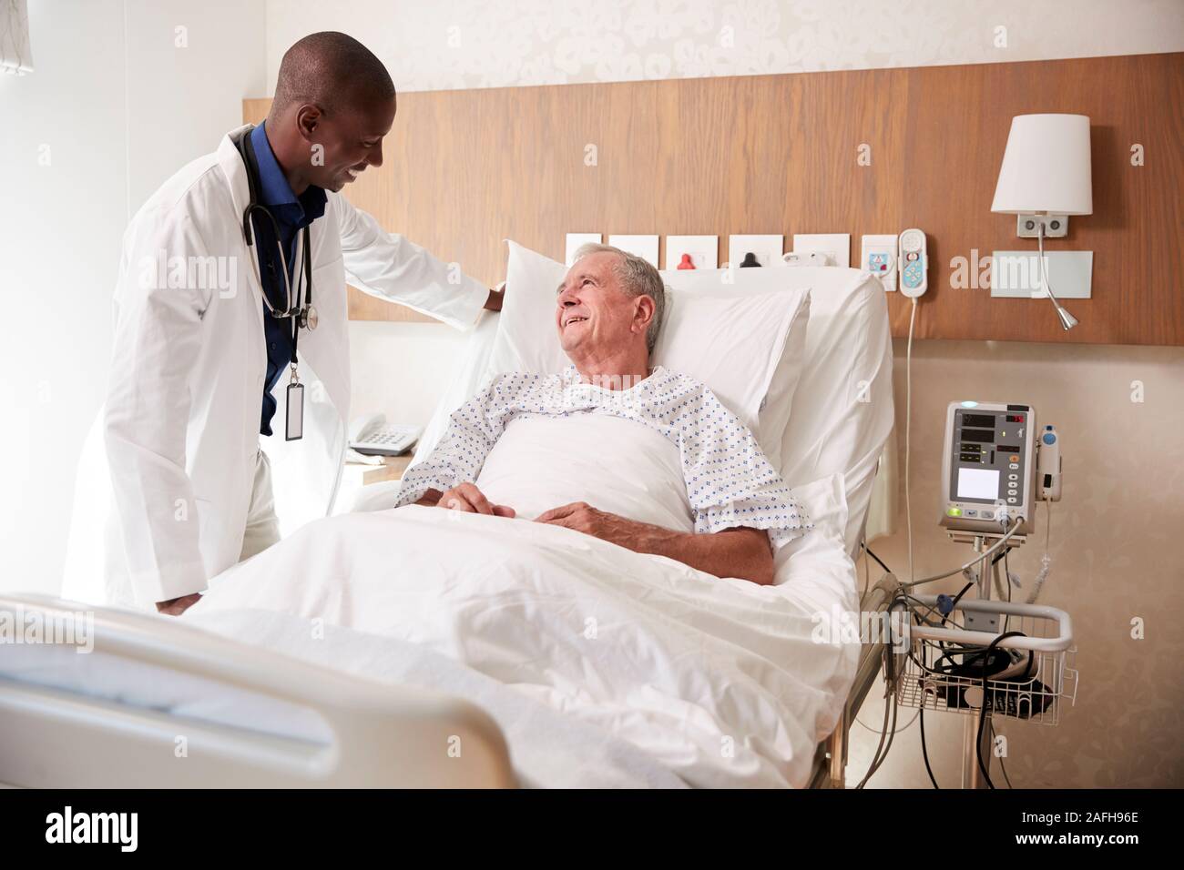 Médecin visiter et parler avec Senior Male Patient In Hospital Bed Banque D'Images