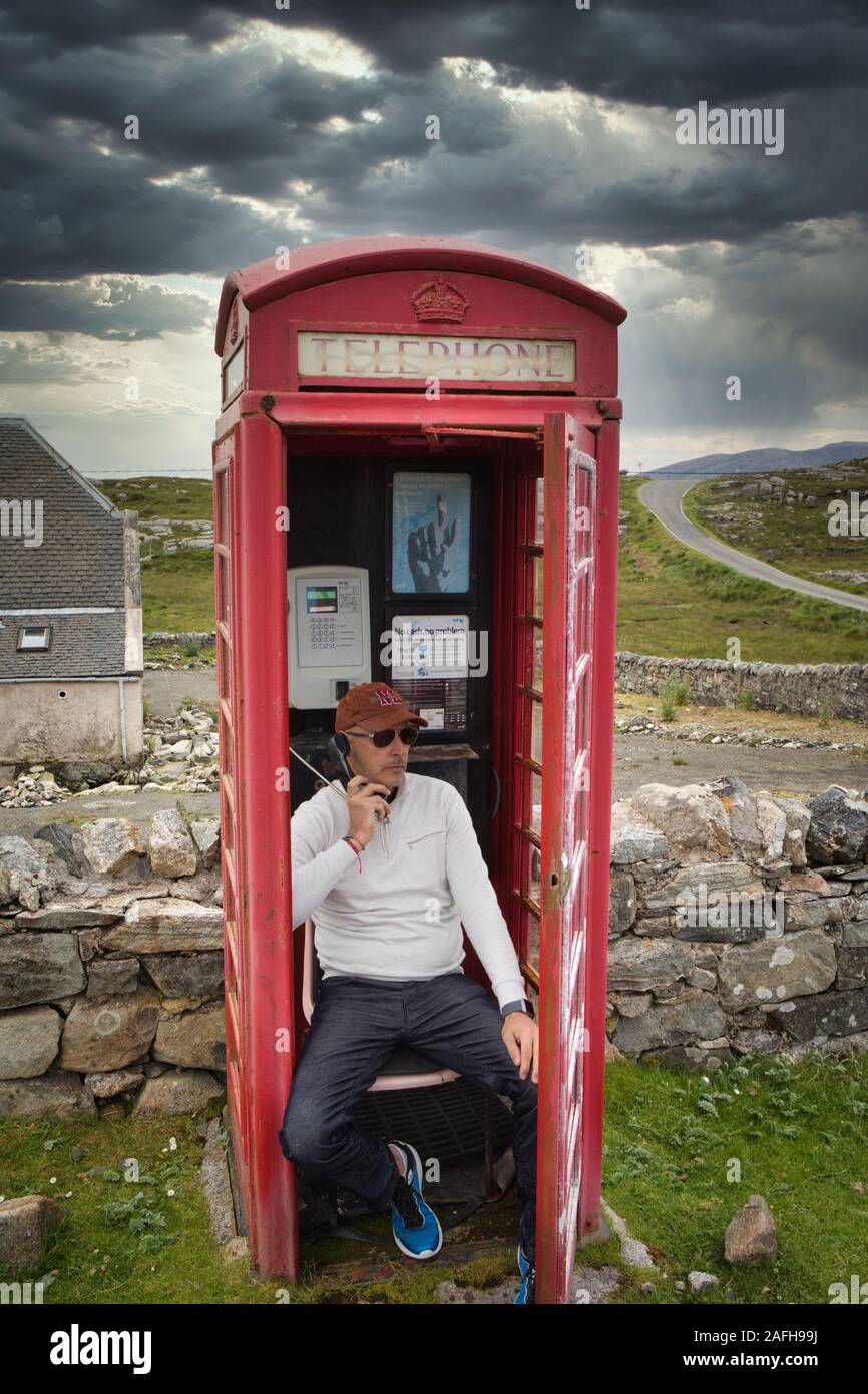 Homme assis dans une boîte de téléphone rouge traditionnelle éloignée ayant une conversation, Isle of Harris, Outer Hebrides, Ecosse Banque D'Images
