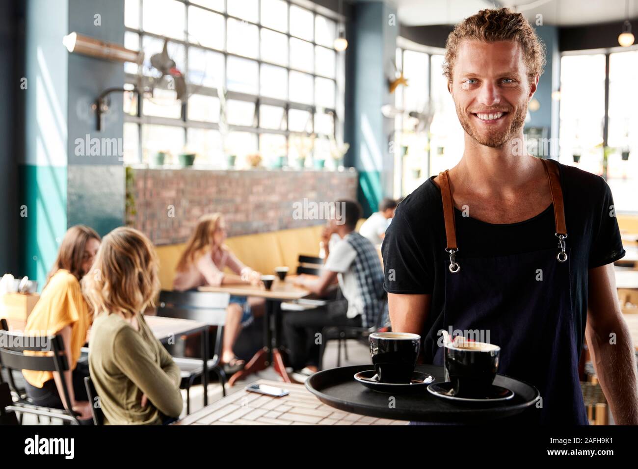 Portrait Of Waiter Serving Customers In Busy Coffee Shop Banque D'Images