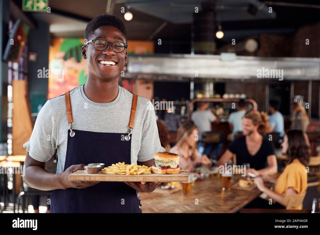 Portrait Of Waiter Serving Food à des clients dans le bar-restaurant animé Banque D'Images