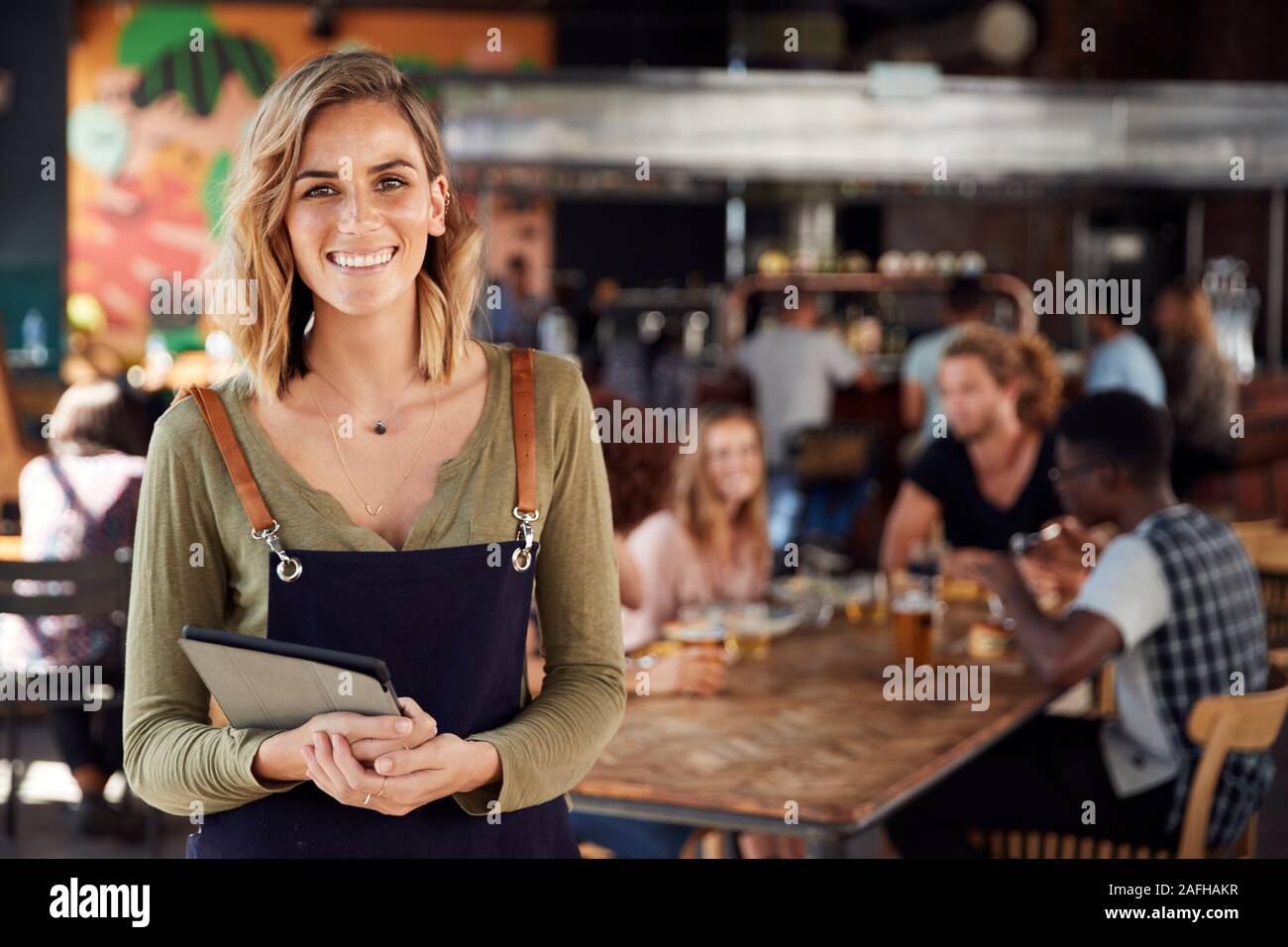 Portrait Of Waitress Holding spéciaux servant Busy Bar Restaurant Banque D'Images