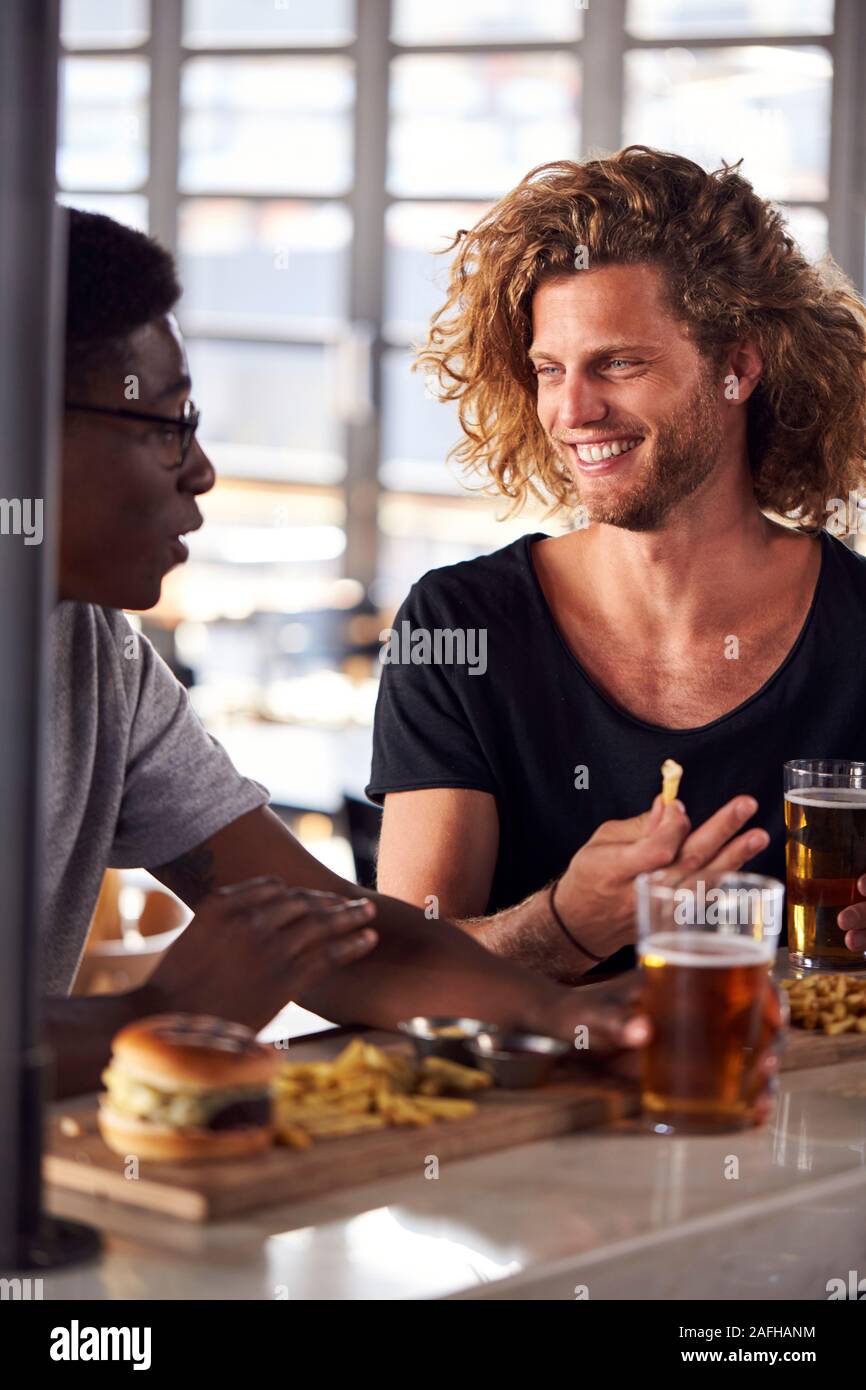 Deux amis de manger de la nourriture et de boire une bière dans un bar sportif Banque D'Images