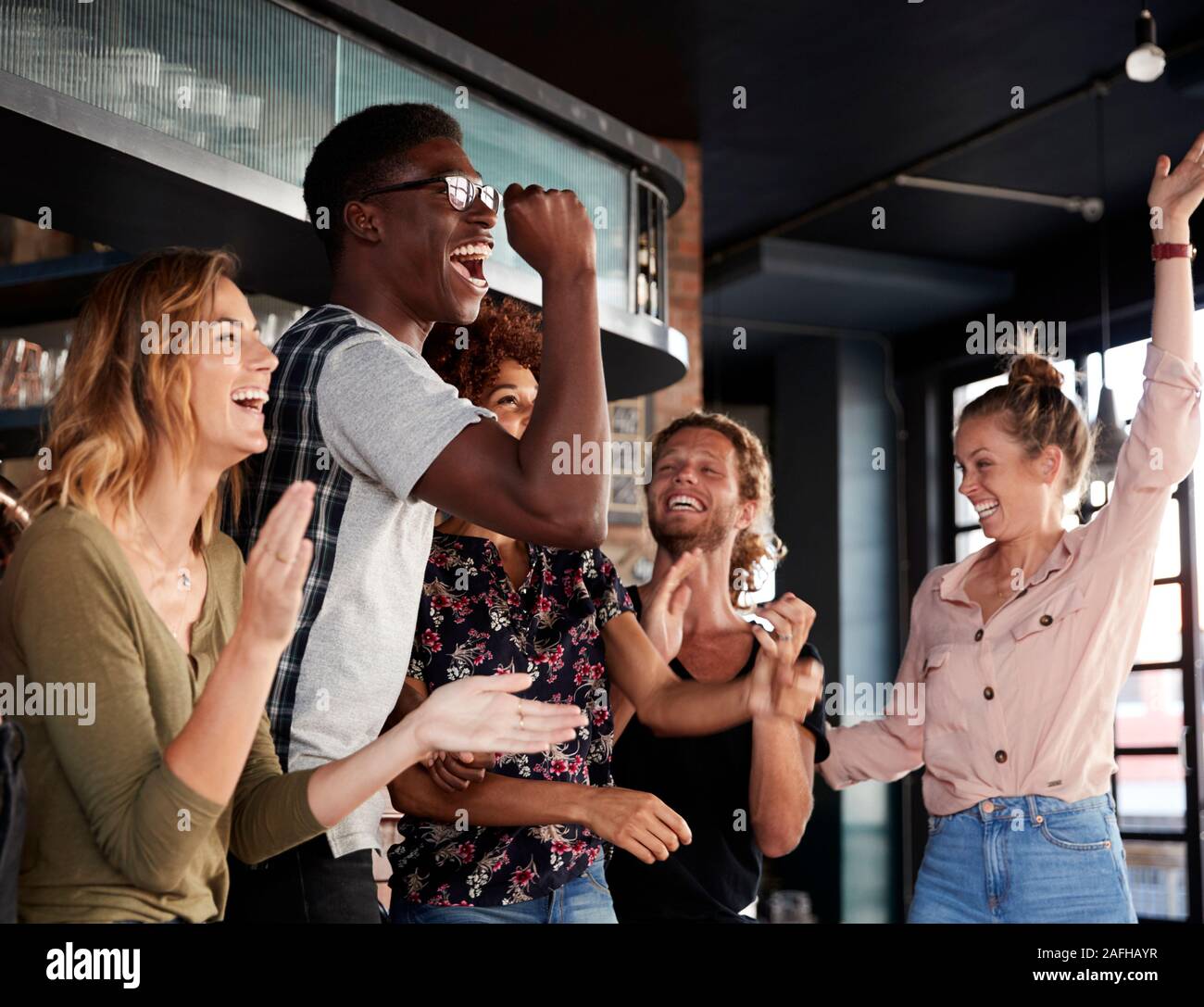 Groupe d'amis masculins et féminins célébrant tout en regardant à l'écran de jeu en Sports Bar Banque D'Images