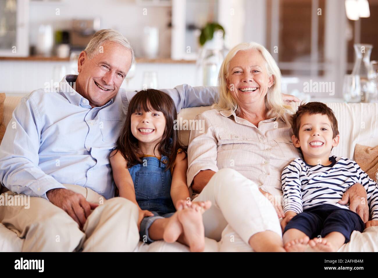 Couple blanc et leurs petits-enfants assis sur un canapé ensemble à la maison smiling to camera Banque D'Images