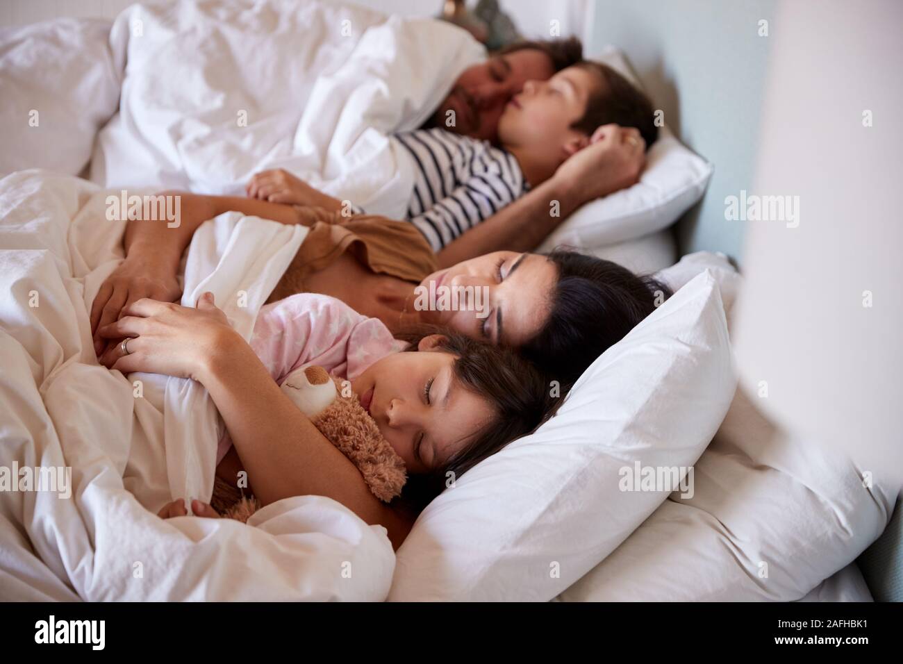 Young parents dormir dans le lit avec leurs deux jeunes enfants, jusqu'à la taille, Close up Banque D'Images