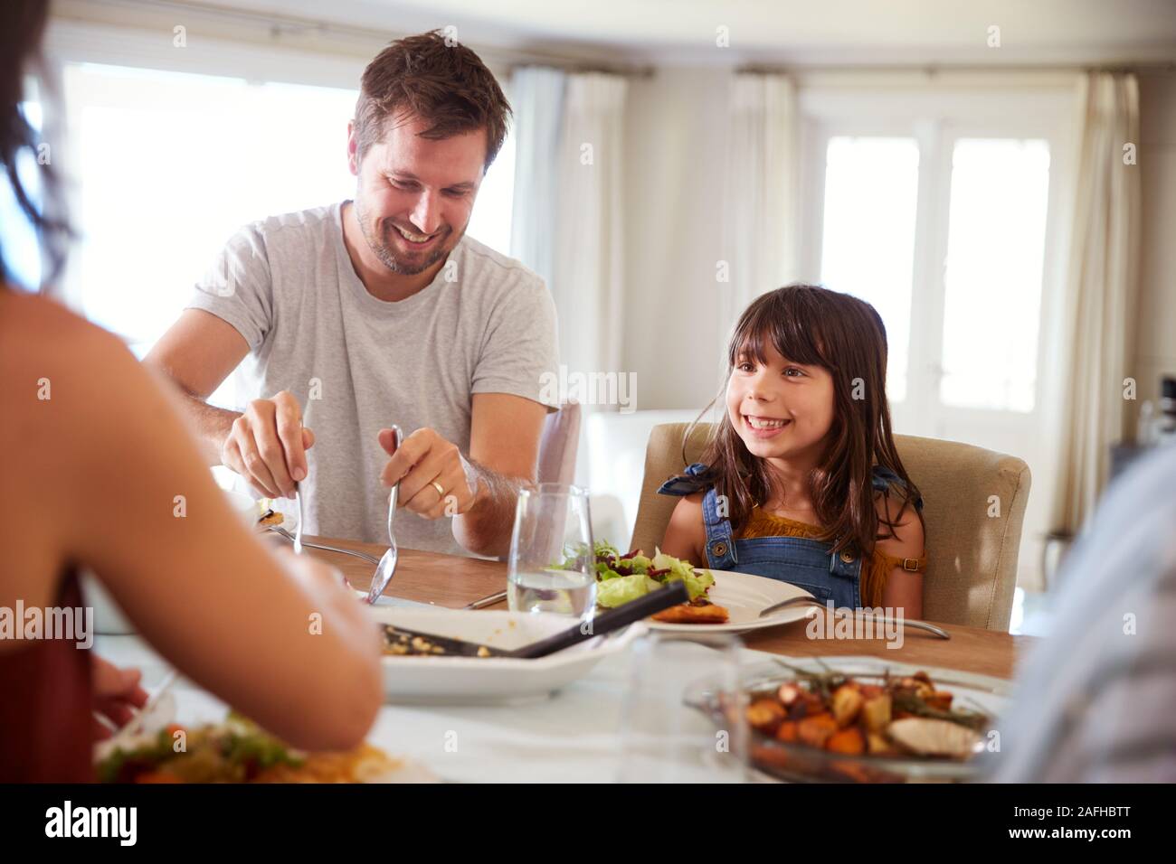 Jeune fille en attente de son père pour servir la nourriture à la table de dîner au cours d'un repas de famille, Close up Banque D'Images