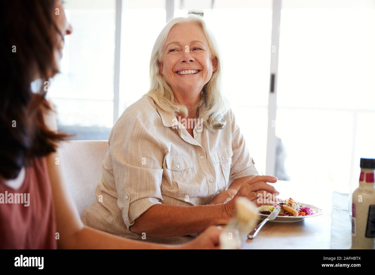 Hauts femme blanche assise à la table de dîner de famille souriant pour sa fille adulte Banque D'Images