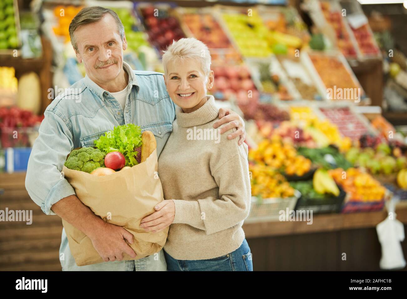 Waist up portrait of smiling senior woman looking at camera tout en profitant de l'épicerie au marché de fermiers, copy space Banque D'Images