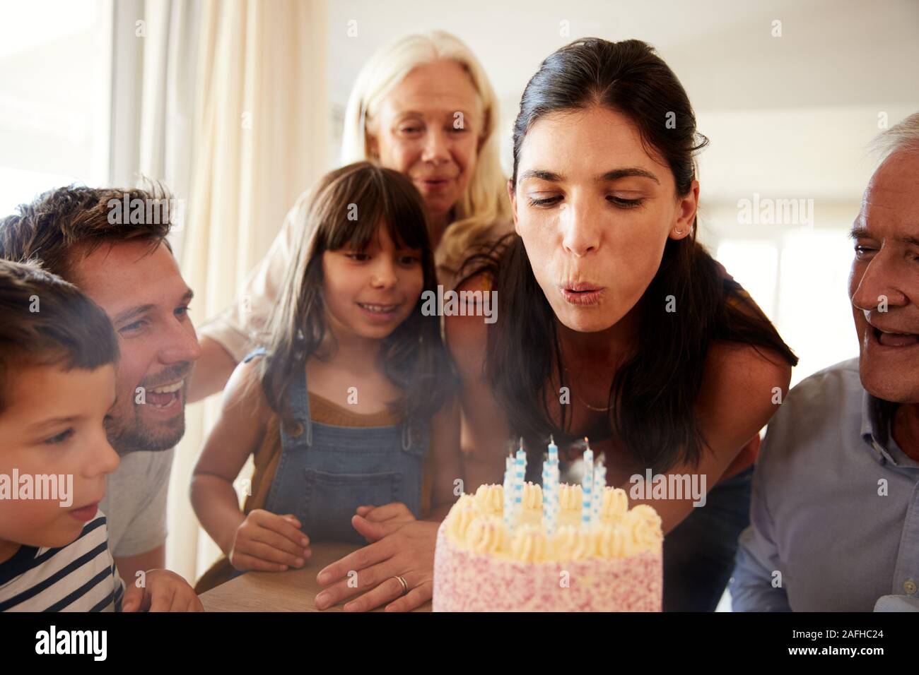 Mid adult blanc femme blowing out candles on cake vu par sa famille, Close up Banque D'Images