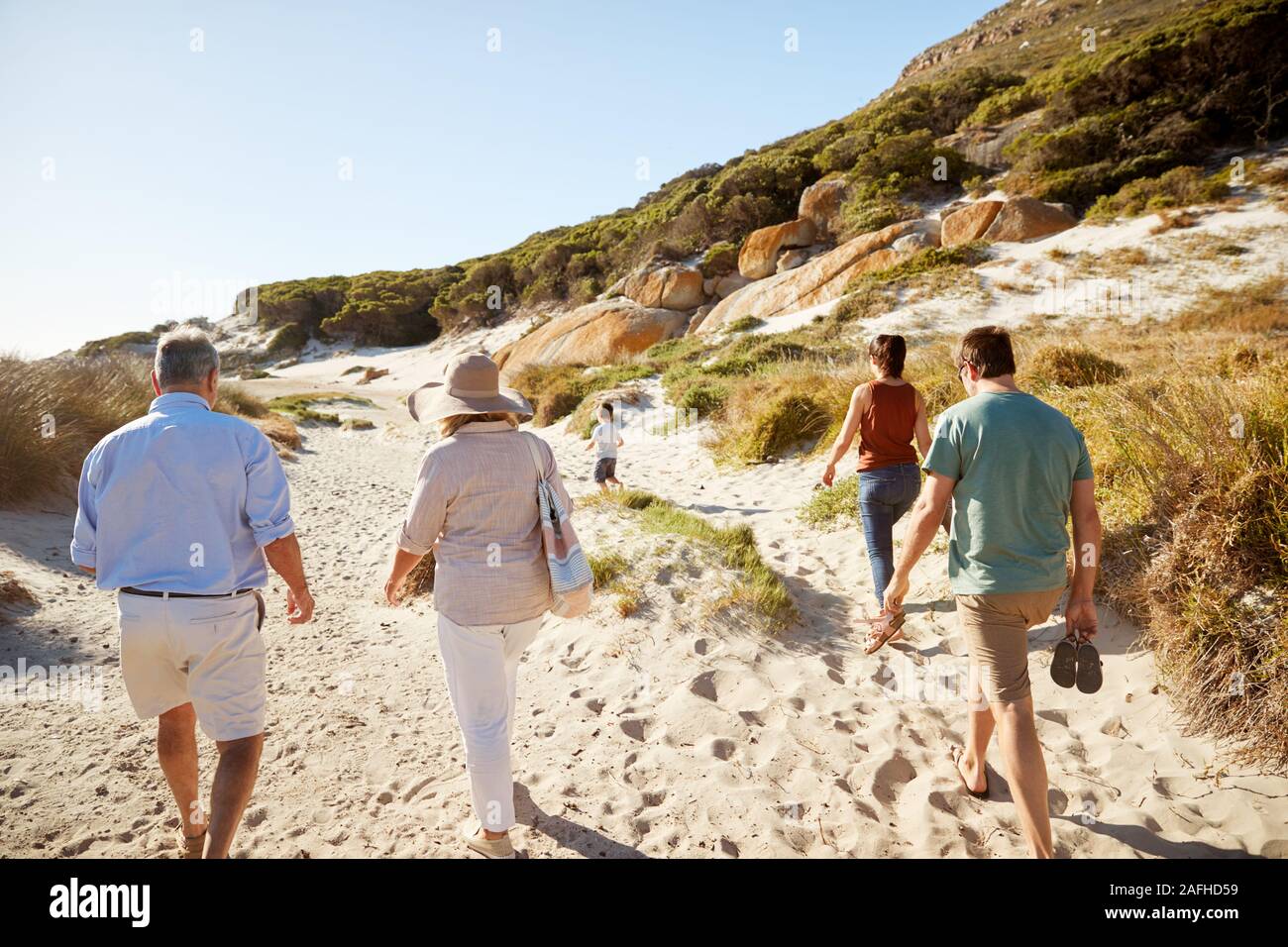 Les parents et grands-parents walking on beach avec jeune garçon en avance sur eux Banque D'Images