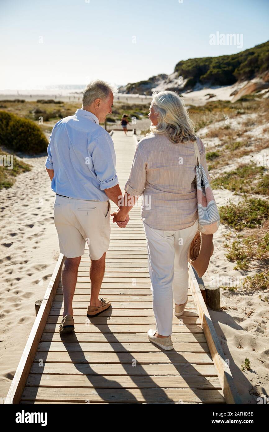 Blanc de la haute couple walking along promenade en bois sur une plage, se tenant la main, pleine longueur, vue arrière Banque D'Images