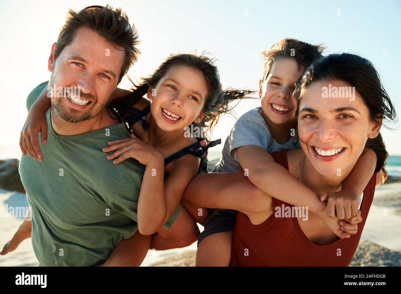 Young parents blanc usurpation de leurs enfants sur une plage, souriant à la caméra, Close up, rétroéclairé Banque D'Images