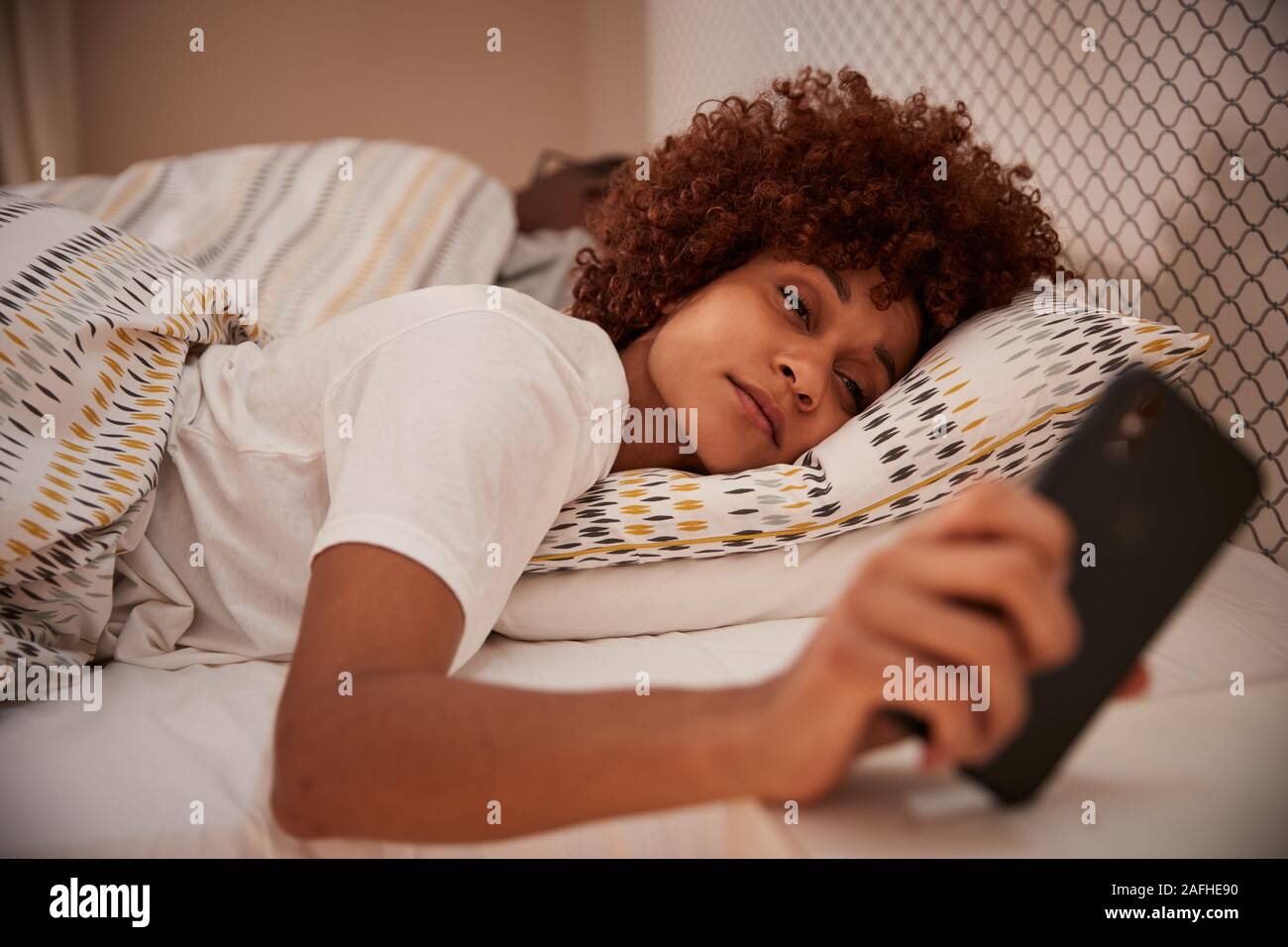 African American Woman millénaire à moitié endormi dans le lit, regardant son smartphone, Close up Banque D'Images