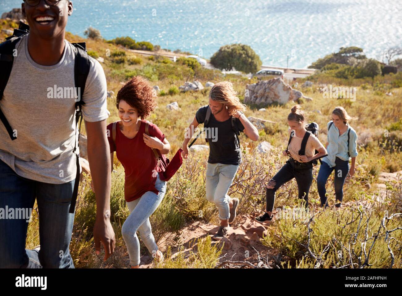 Les amis des jeunes adultes randonnées seul fichier en montée sur un chemin par la côte, pleine longueur Banque D'Images