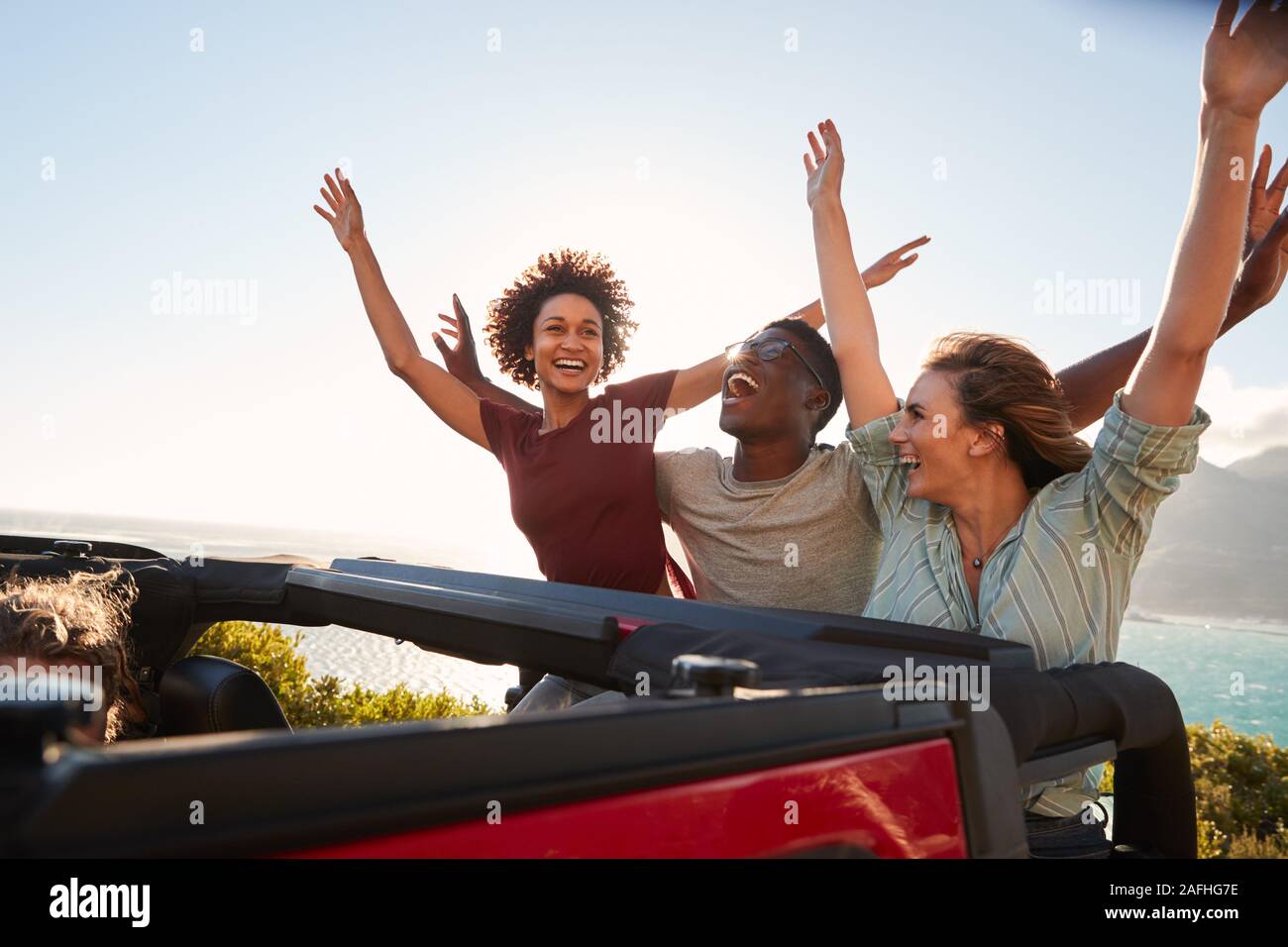 Millénaire excité amis voyageant à l'arrière d'une voiture ouverte avec les bras en l'air Banque D'Images