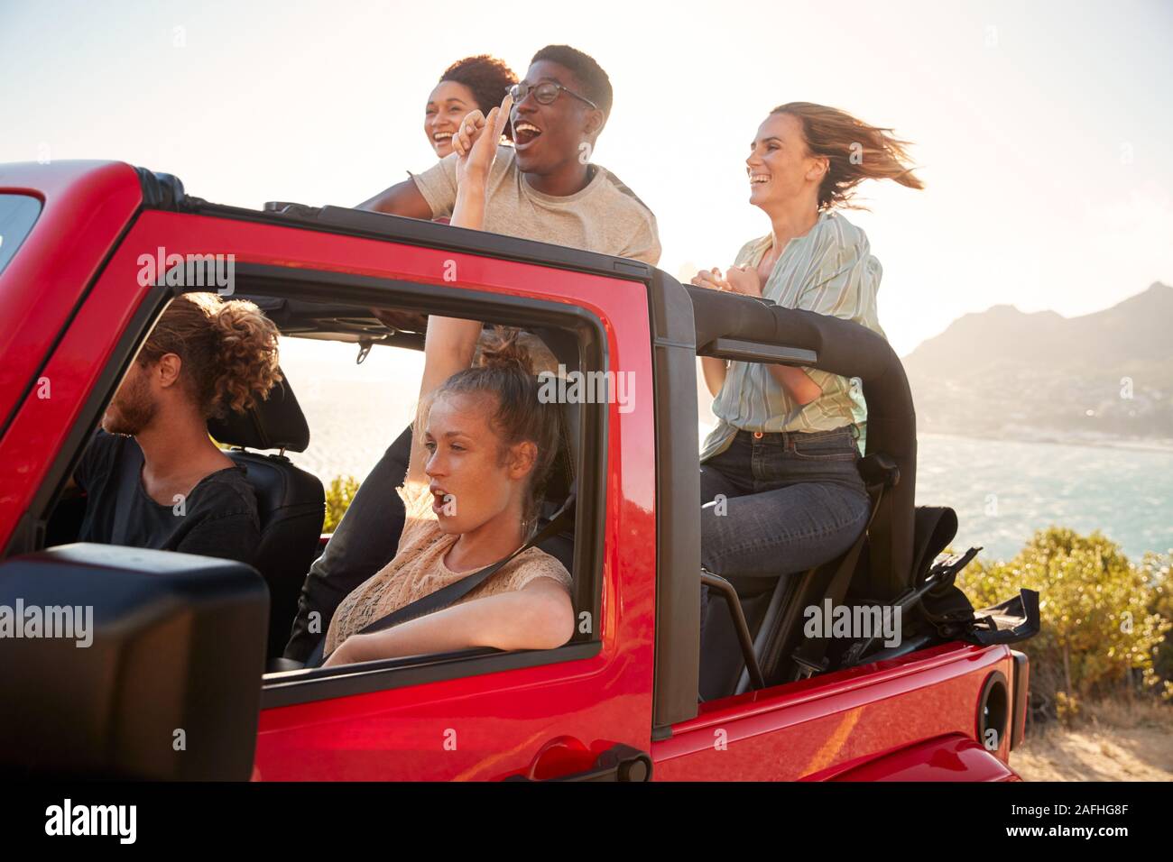 Cinq jeunes amis adultes sur un voyage sur la route au volant d'1h30 en jeep par la mer Banque D'Images