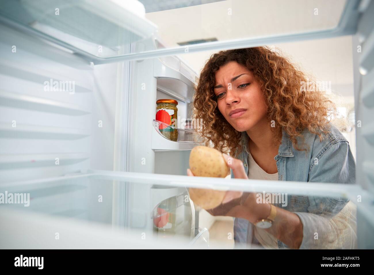 Femme déçu à la l'intérieur réfrigérateur vide sauf pour la pomme de terre sur la tablette Banque D'Images