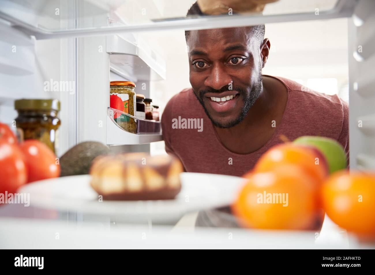 À la vue de l'intérieur du réfrigérateur que l'homme ouvre la porte et atteint pour Donut malsain Banque D'Images