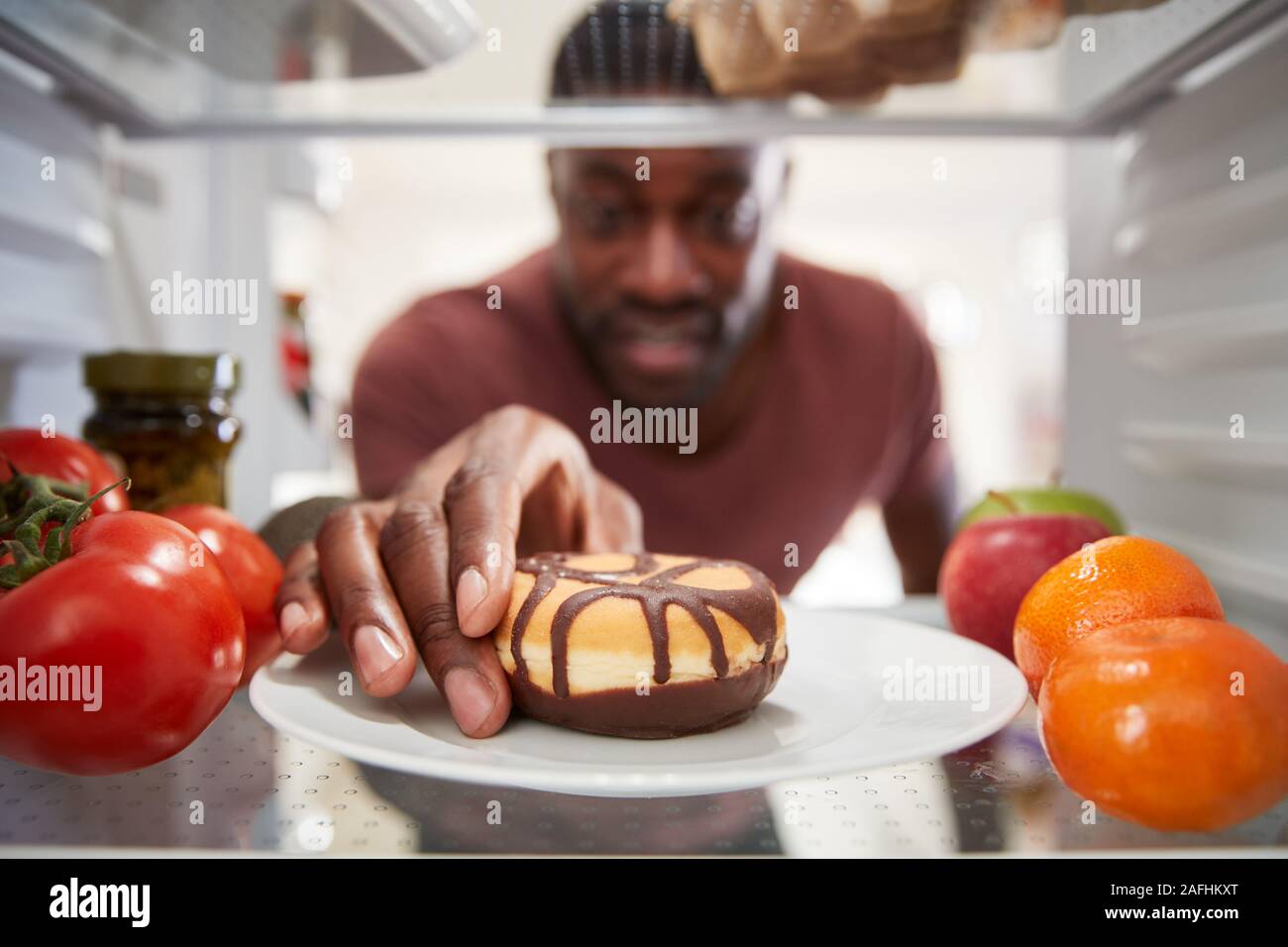 À la vue de l'intérieur du réfrigérateur que l'homme ouvre la porte et atteint pour Donut malsain Banque D'Images