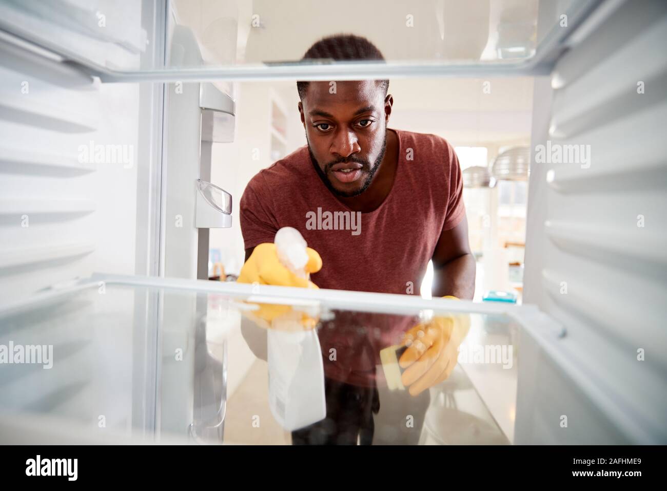 À la vue de l'intérieur réfrigérateur vide que l'Homme portant des gants de caoutchouc nettoie Etagères Banque D'Images