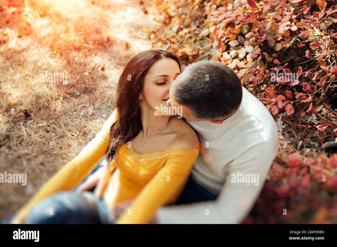 Couple amoureux assis sur l'automne les feuilles tombées dans un parc, bénéficiant d'une belle journée d'automne. L'homme s'embrasser une femme dans un front Banque D'Images