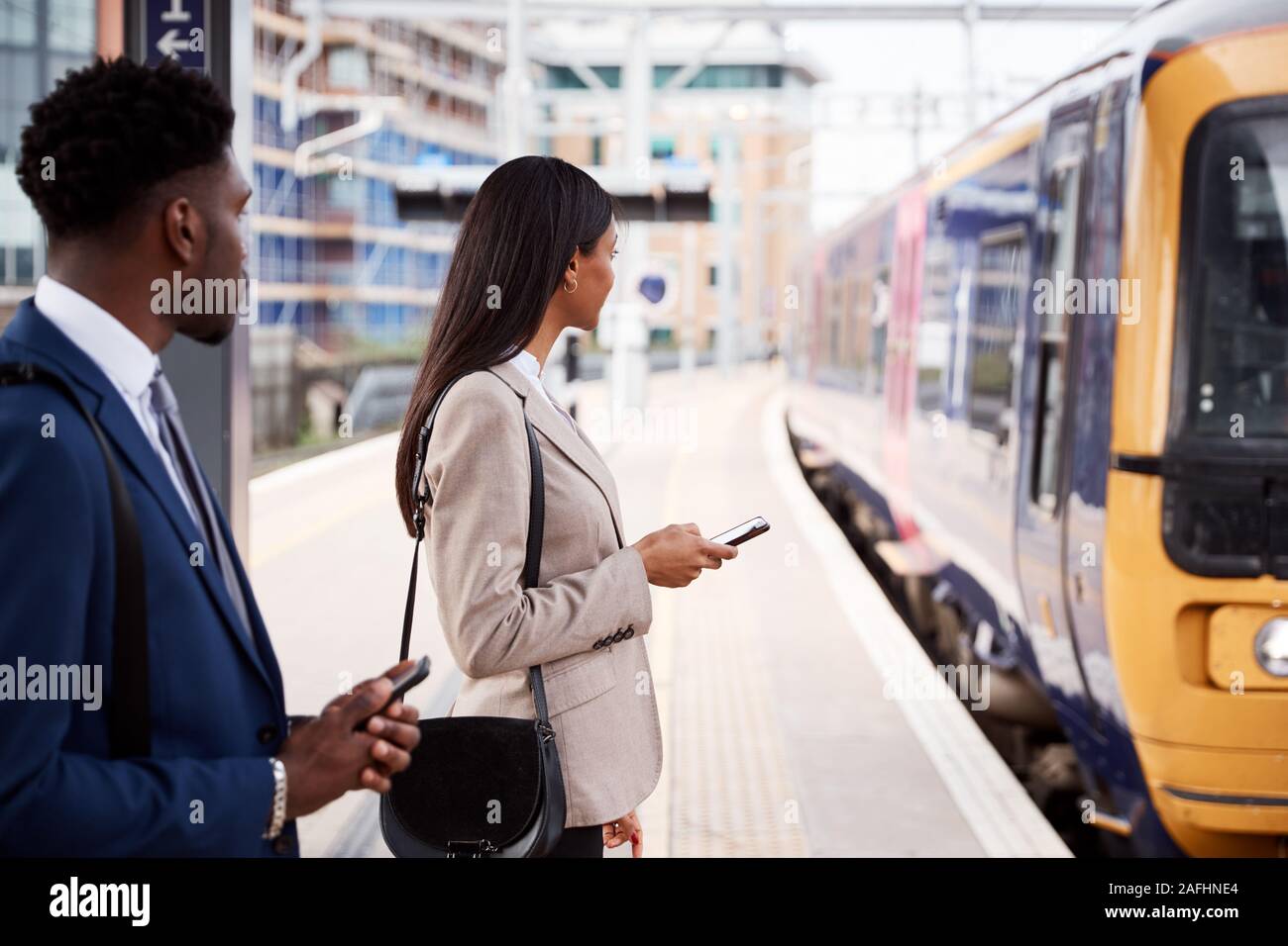 Businessman And Businesswoman pour se rendre à son travail sur un quai de gare en attente de Train Banque D'Images