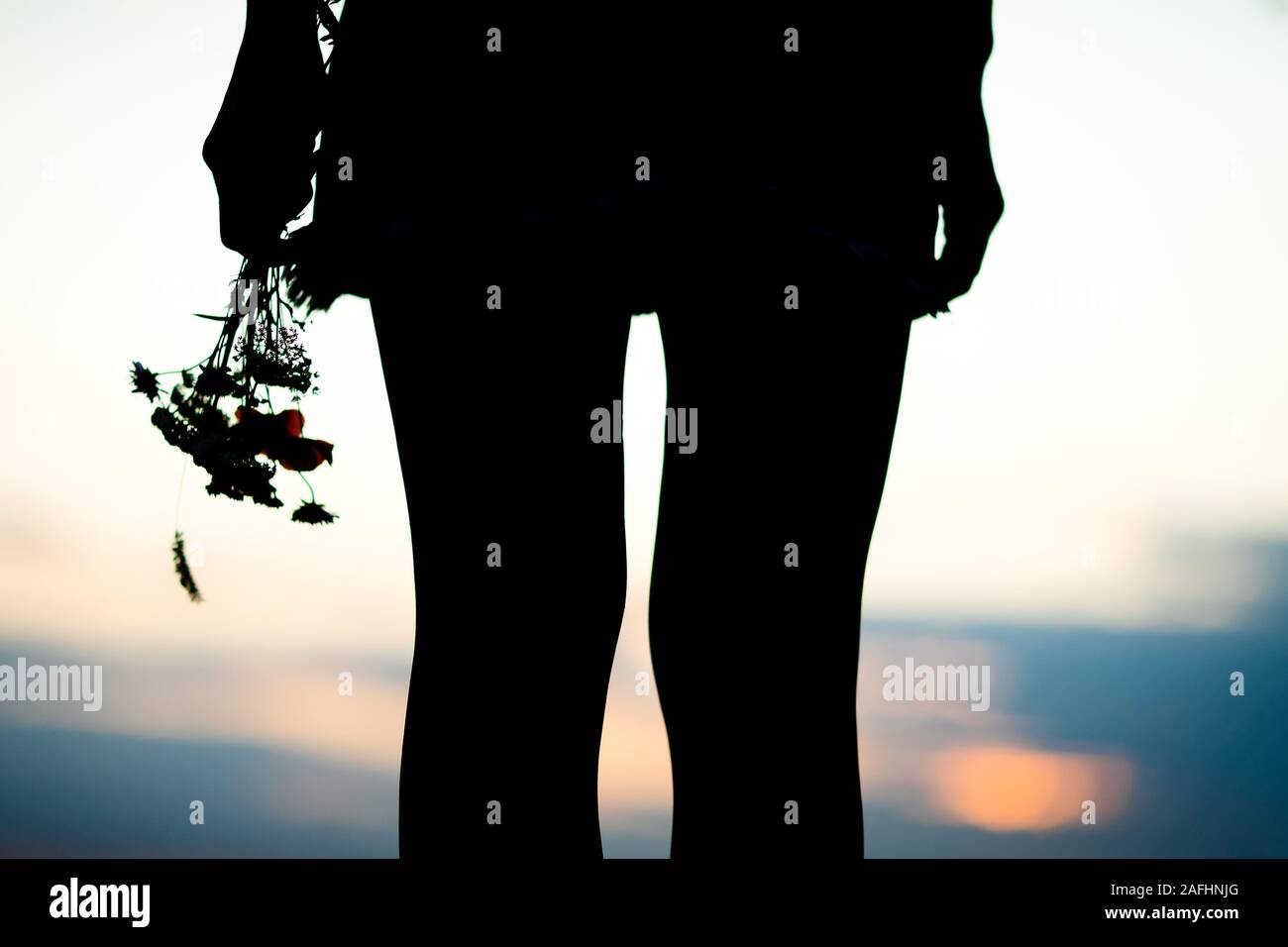 Les jambes de la jeune femme et bouquet de fleurs des prés, silhouette contre le coucher du soleil Banque D'Images
