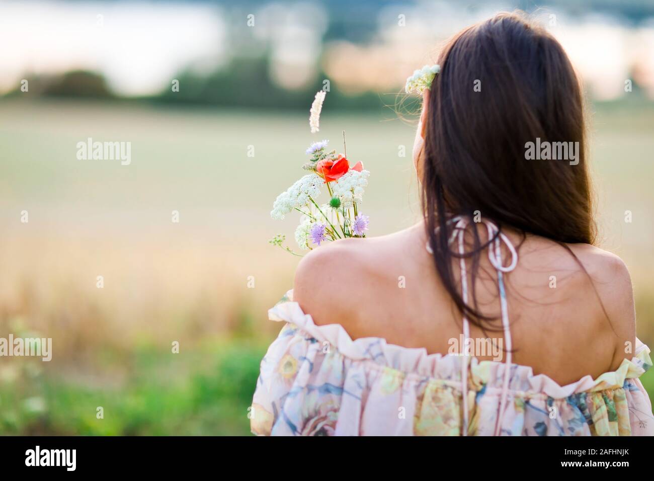 Vue arrière de jeune femme habillé en tenue d'été ont bouquet de fleurs des prés pendant l'heure du coucher du soleil Banque D'Images