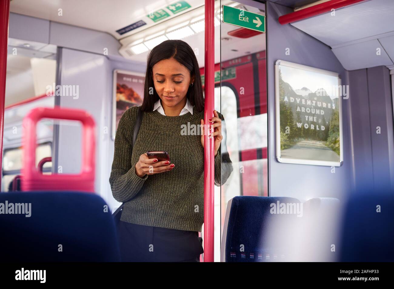 Femme Debout de passagers par portes en train Looking At Mobile Phone Banque D'Images