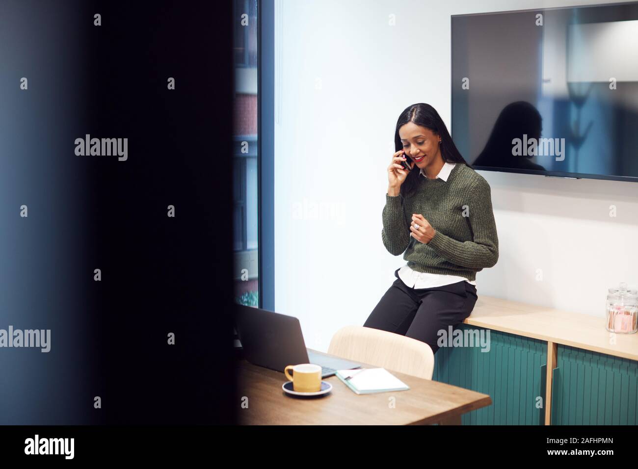 Businesswoman Sitting on Desk in Meeting Room Talking On Mobile Phone Banque D'Images