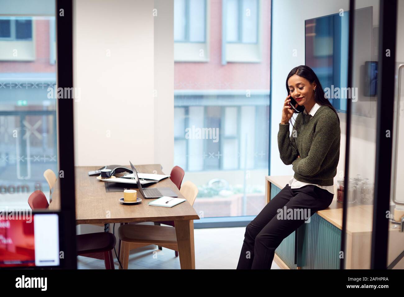 Businesswoman Sitting on Desk in Meeting Room Talking On Mobile Phone Banque D'Images