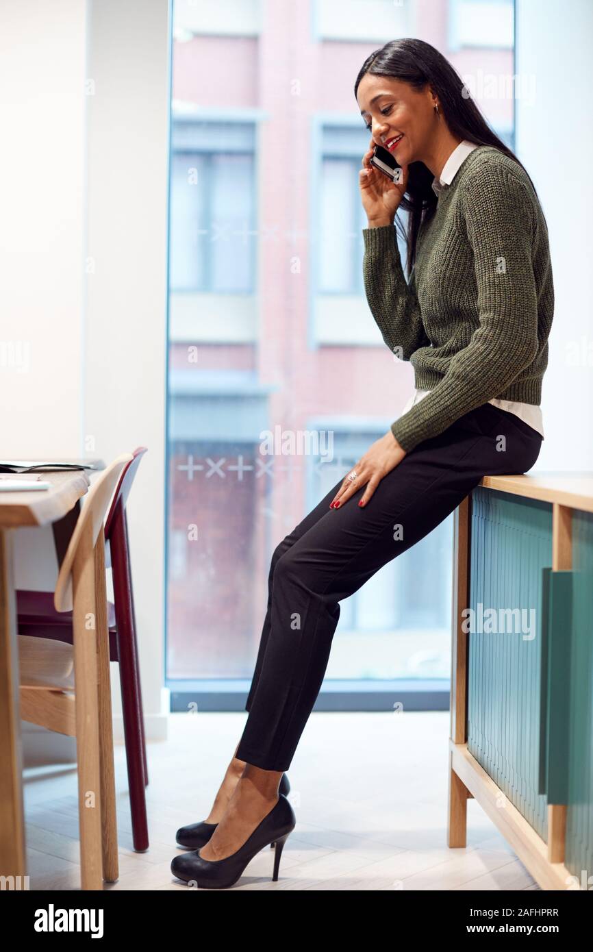 Businesswoman Sitting on Desk in Meeting Room Talking On Mobile Phone Banque D'Images