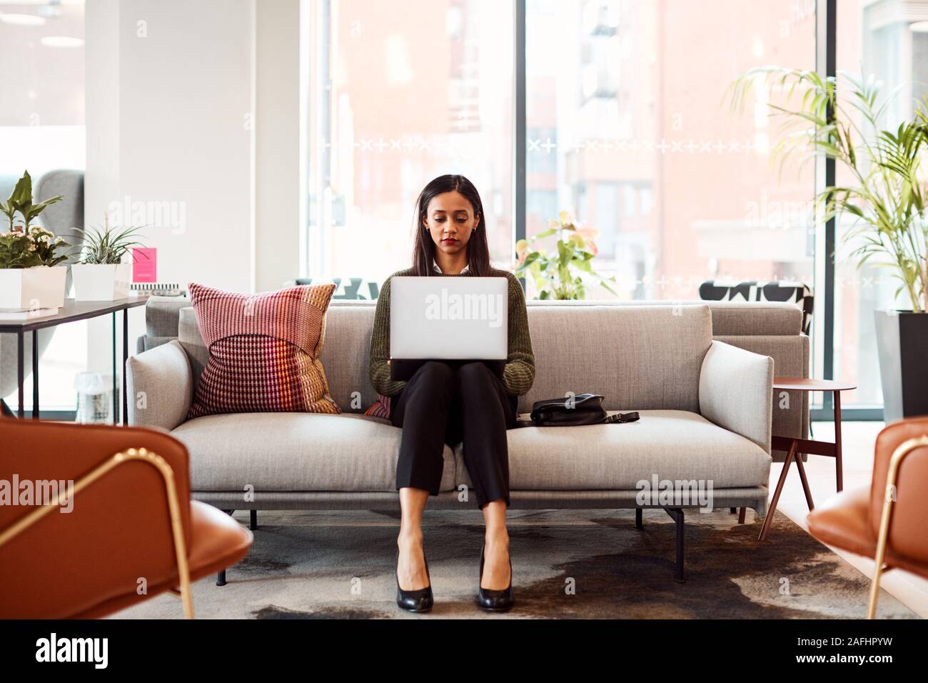 Businesswoman Sitting on Sofa Working On Laptop In Office d'espace de travail partagé Banque D'Images