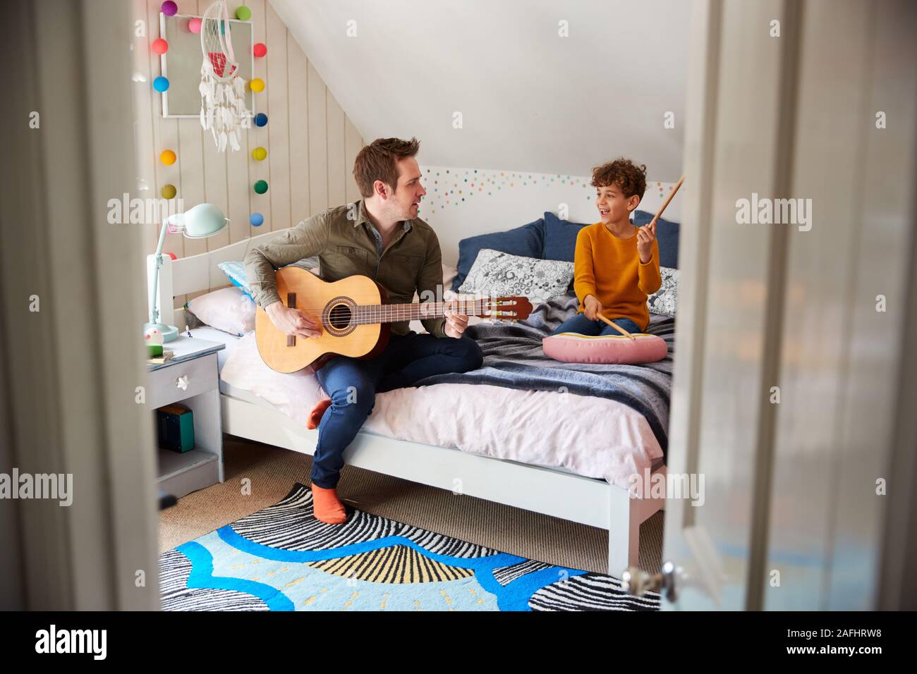 Père seul à jouer de la guitare avec fils qui batterie le coussin dans la chambre Banque D'Images