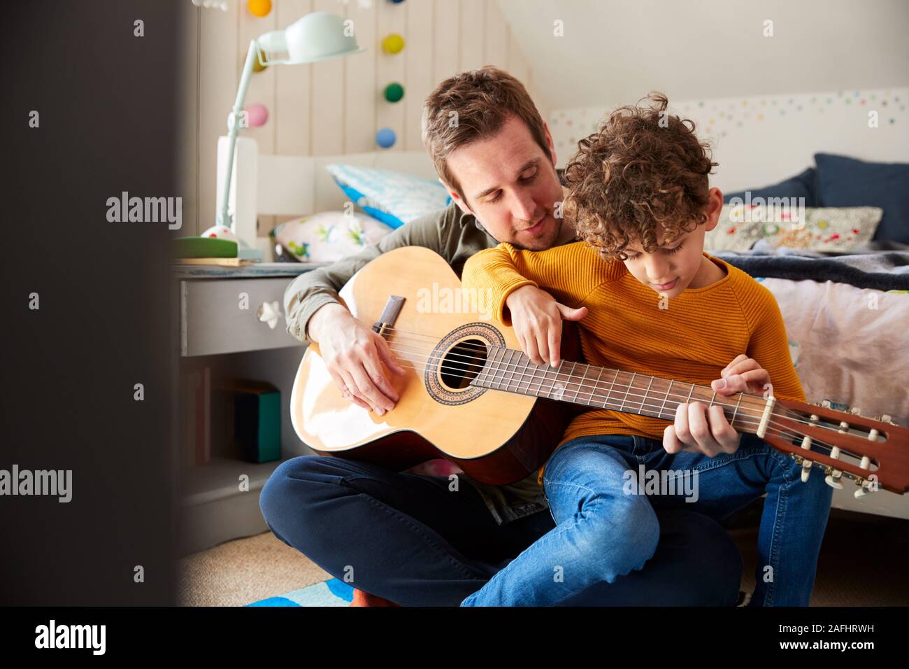 Père seul à la maison avec son fils lui apprenant à jouer de la guitare acoustique dans la chambre Banque D'Images